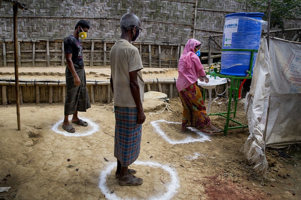 A woman using a contactless handwashing station while two people line up at a distance.